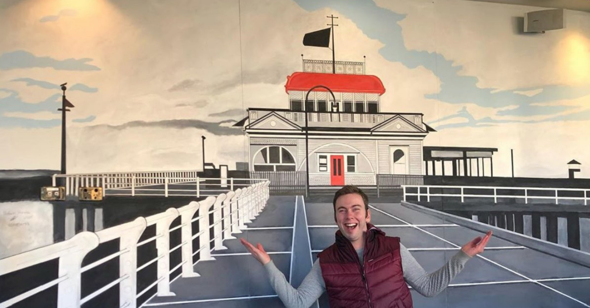 A man smiling on a deck with room in back.