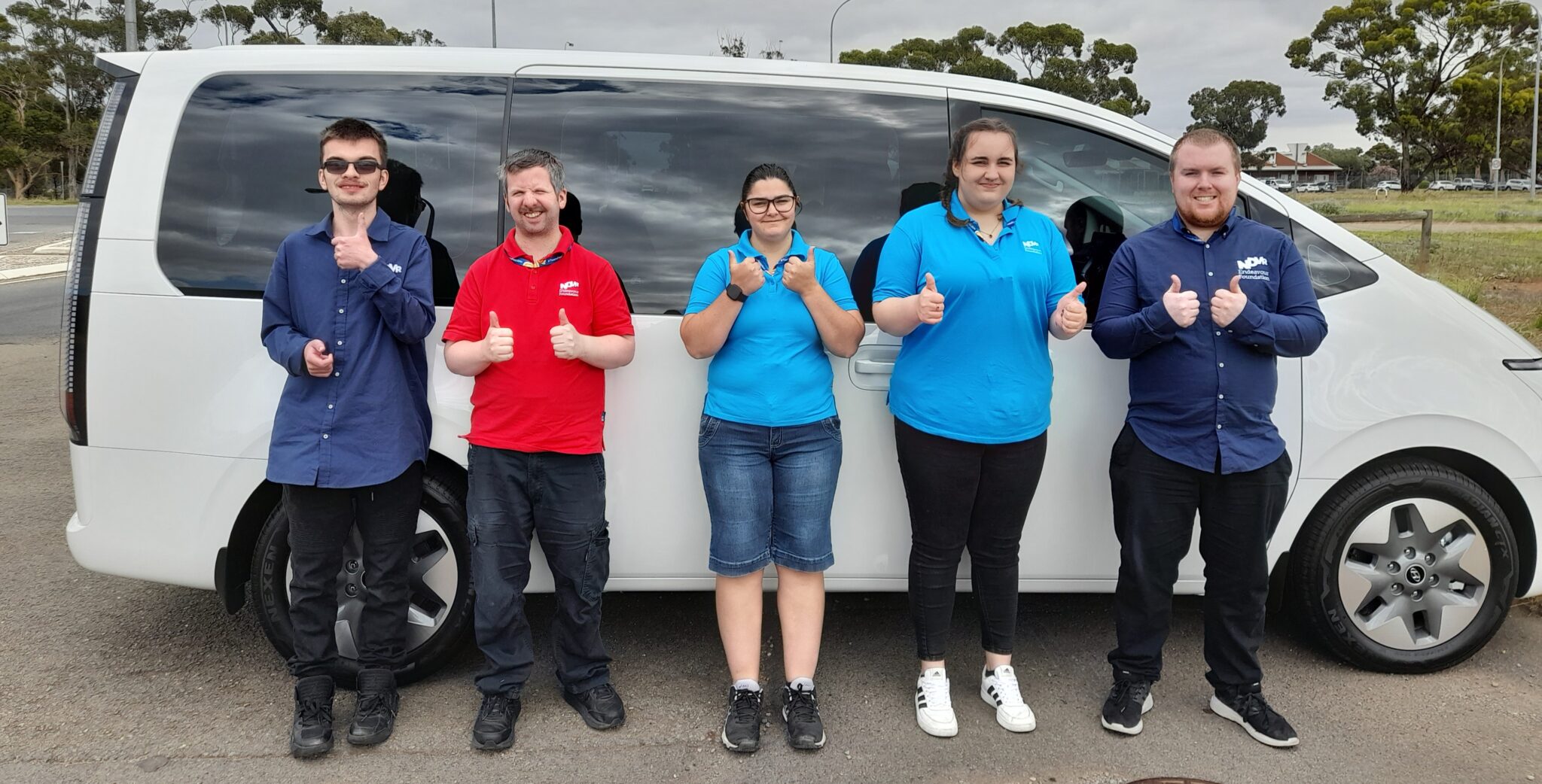 3 Men and 2 women standing with a van smiling with thumbs up.