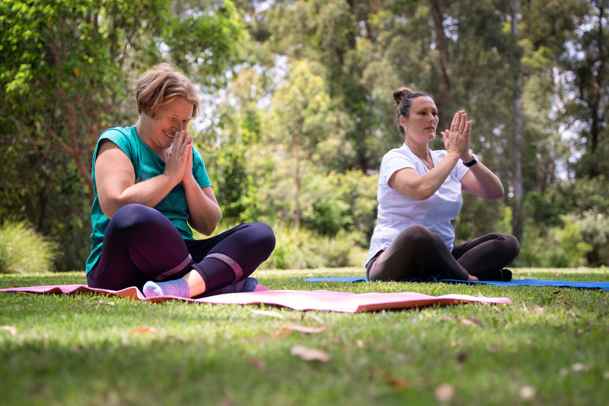 2 Women learning yoga. One of them is smiling, and the other is in the zone.