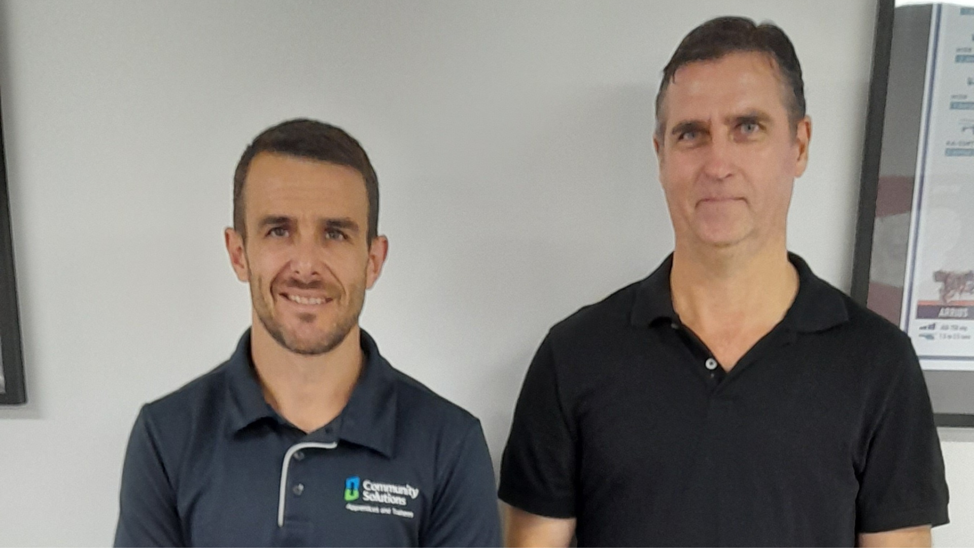 2 Man from Community Solutions standing at the wall with a smile getting their photo taken.