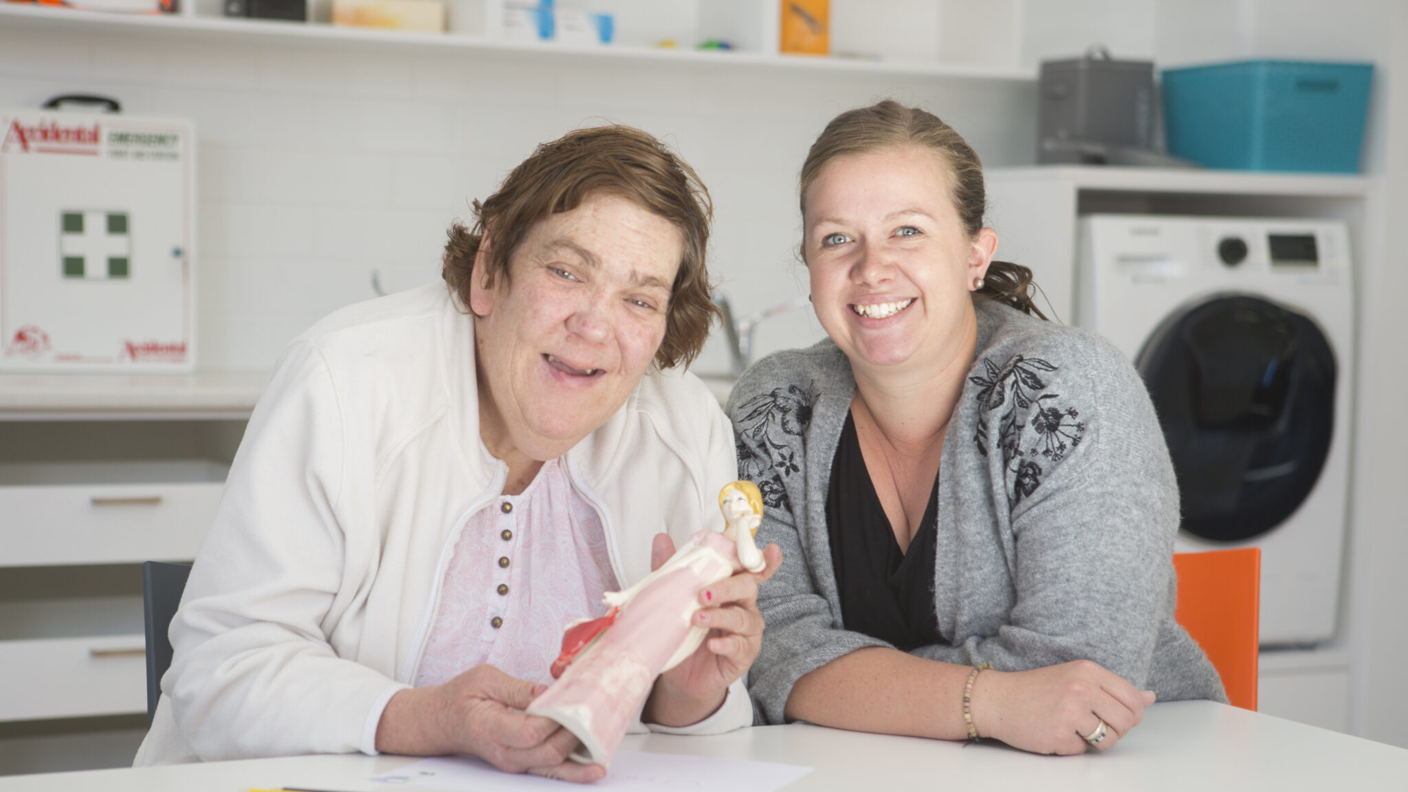 Woman with a support worker in a home showing her doll.