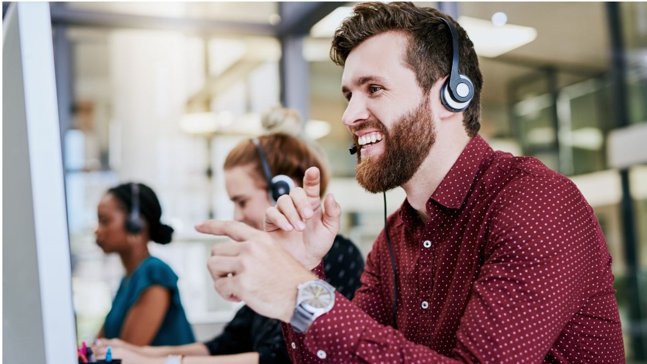 2 Women and 1 man who is smiling while at the computer with their headsets on.