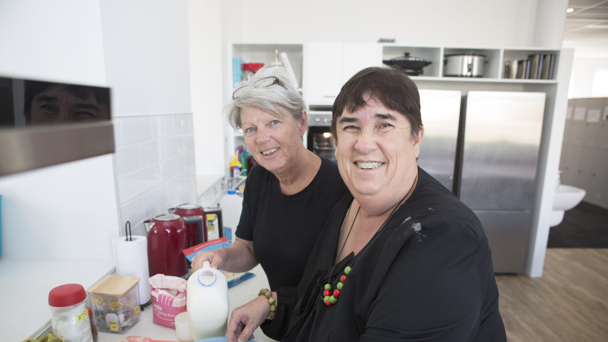 Women in the kitchen with the help of support worker learning to cook.