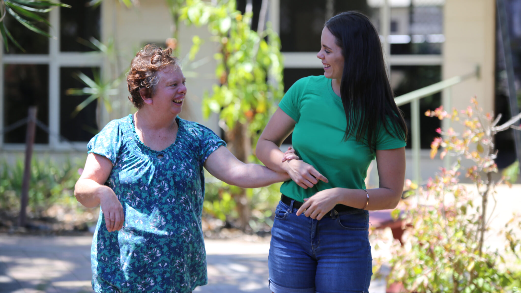 Women with a support worker holding hands and going for a walk outside.
