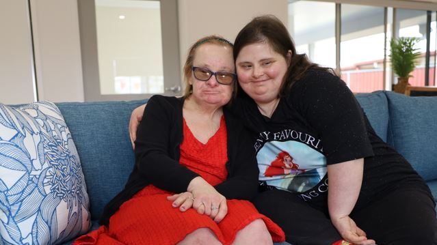 Two women sitting on a couch hugging each other.