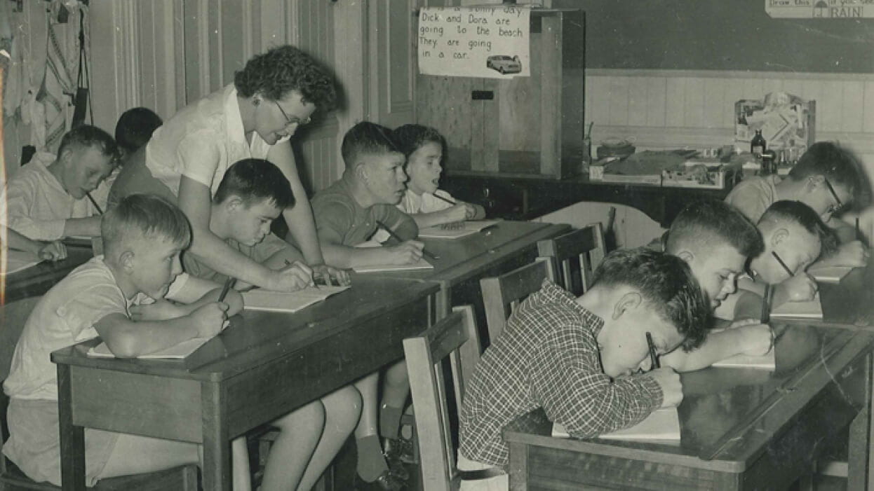 A teacher supports children as they write in their books.